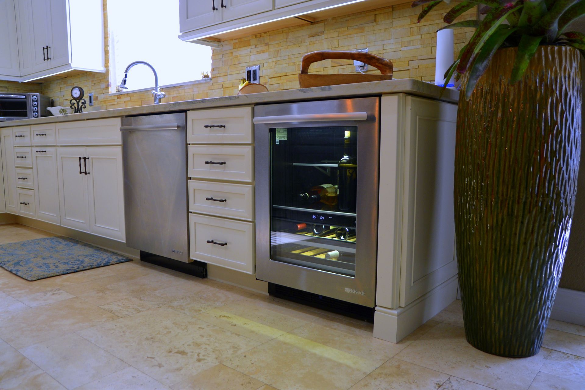 Modern kitchen with stainless steel dishwasher, wine fridge, white cabinets, and a large potted plant