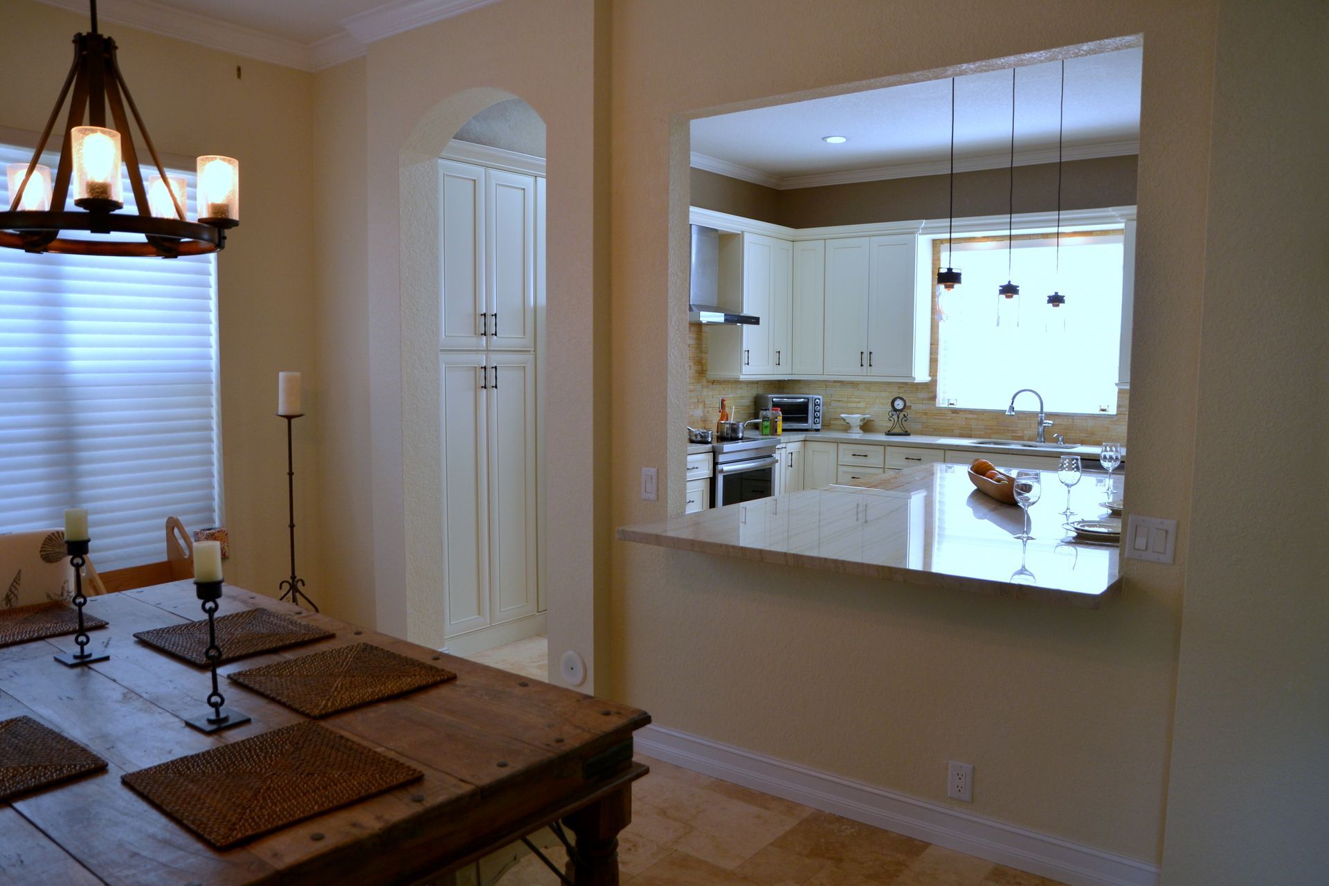 Dining room opening into a bright kitchen with beige walls, a wooden table, and hanging light fixture