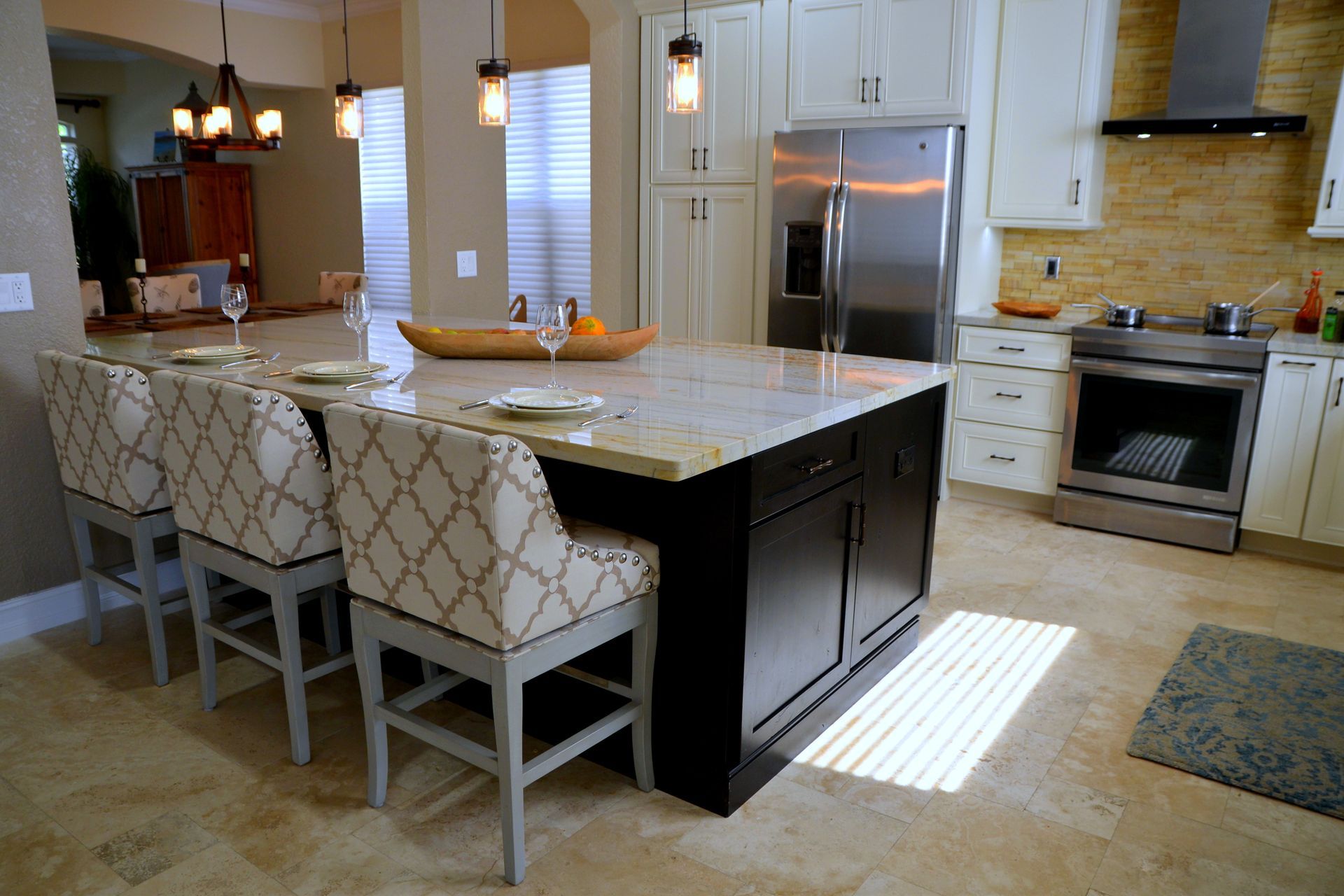 Modern kitchen with marble island, patterned chairs, stainless fridge, and sunlit tile floor
