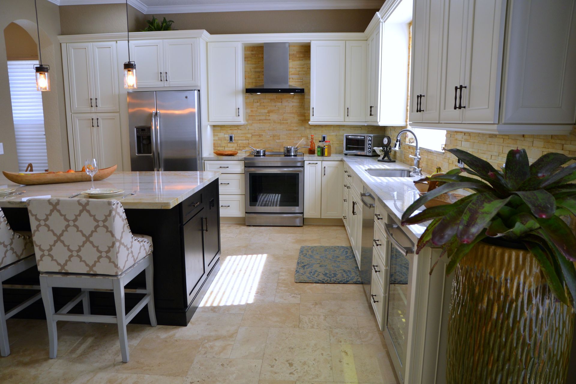 Bright kitchen with white cabinets, marble island, stainless fridge, and a potted plant in the foreground