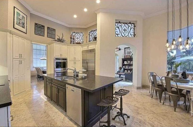 Bright open kitchen with island, dark countertops, bar stools, and adjacent dining area with chandelier.