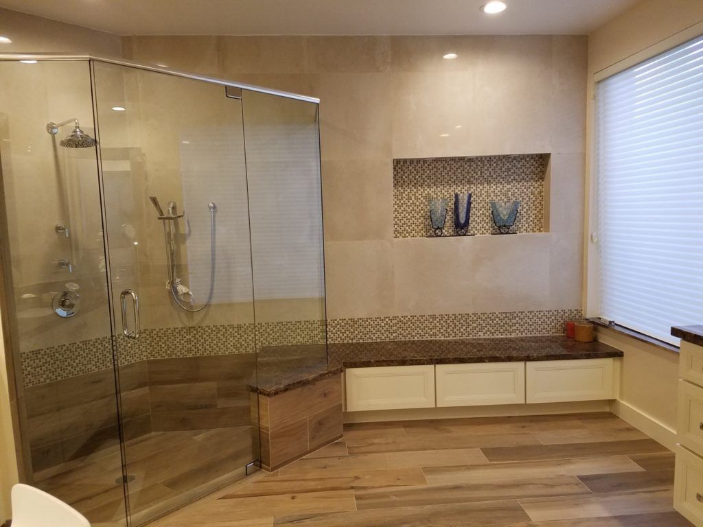 Modern bathroom with glass shower, built-in bench, beige tile, wood-look flooring.