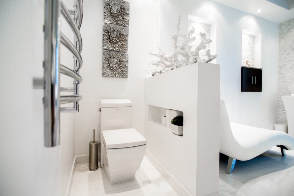 Modern white bathroom with towel rack, square toilet, and decorative wall art.
