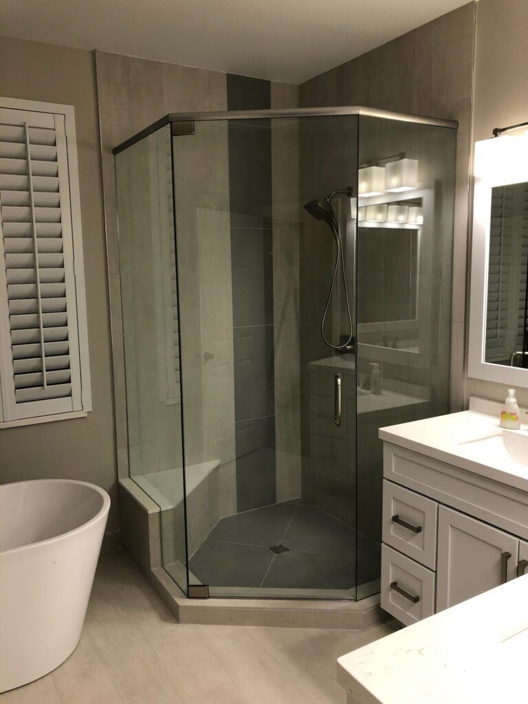 Modern bathroom with a glass-enclosed shower, freestanding tub, and a vanity. Light gray and white tones.