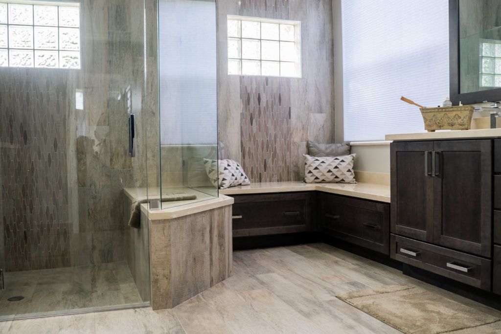 Spacious bathroom with glass shower, built-in bench seating, dark cabinetry, and neutral-toned stone tile.