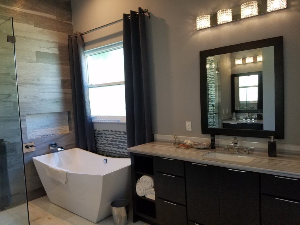 Modern bathroom with freestanding tub, dark vanity, large mirror, and window with blue drapes.