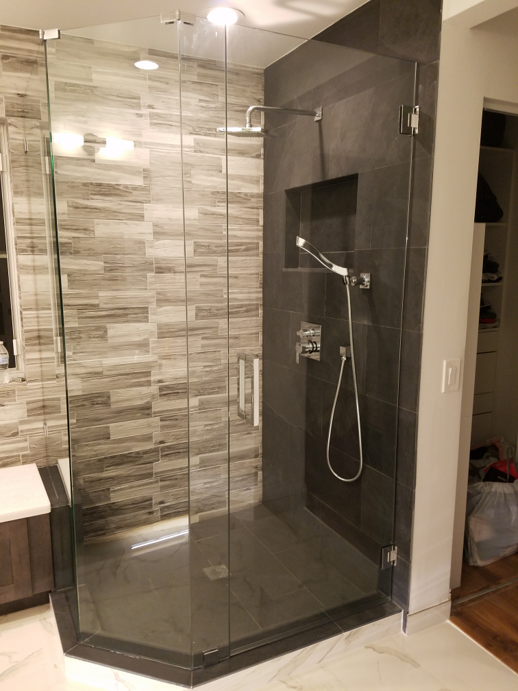 A modern shower with gray tile, glass doors, and a built-in shelf.
