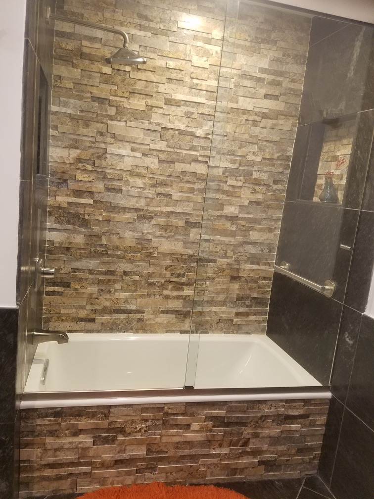 Shower and bathtub combo with stone tile surround and clear glass panels.