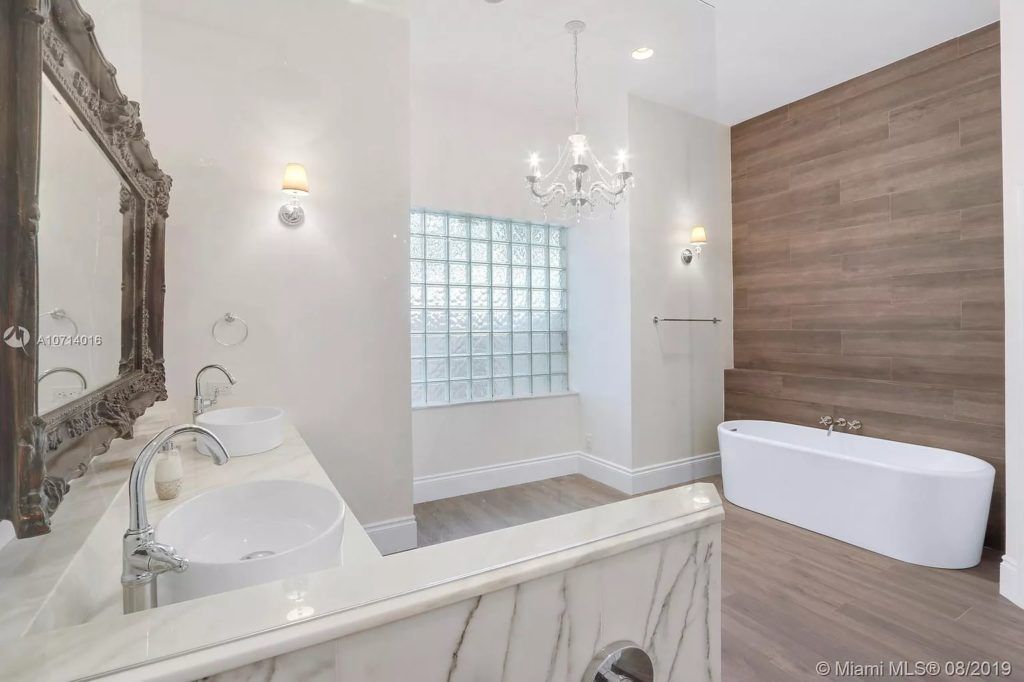 Luxurious bathroom with marble counters, ornate mirror, chandelier, and a freestanding tub.
