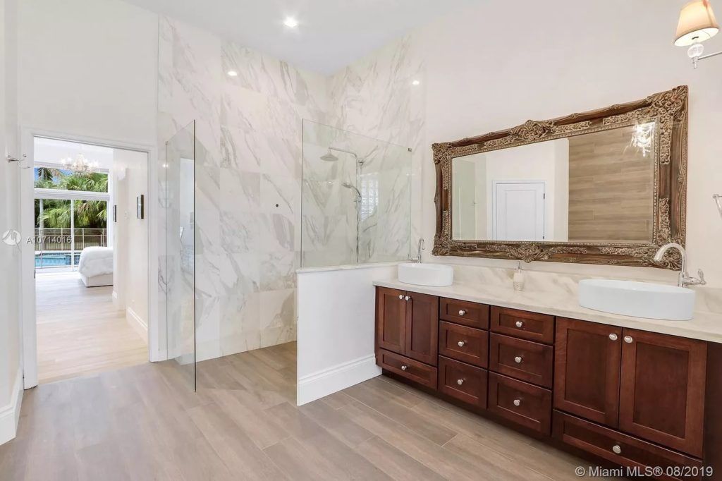 Luxury bathroom with marble shower, double vanity, and large mirror. Light wood flooring.