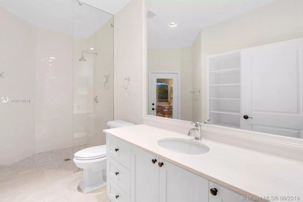 White bathroom with a shower, vanity, toilet, and large mirror.