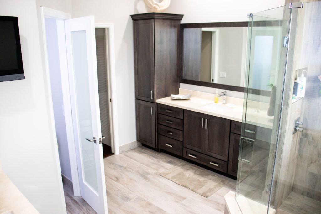 Bathroom with dark wood vanity, large mirror, glass shower, and open door.