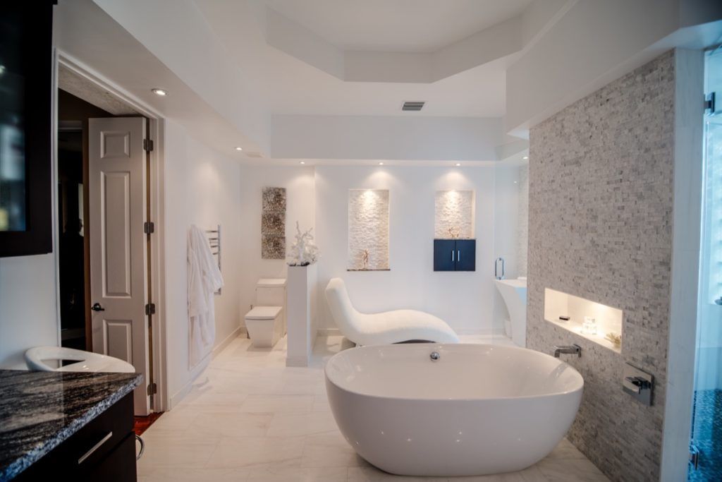 Luxurious white bathroom with a soaking tub, chaise lounge, and marble walls.