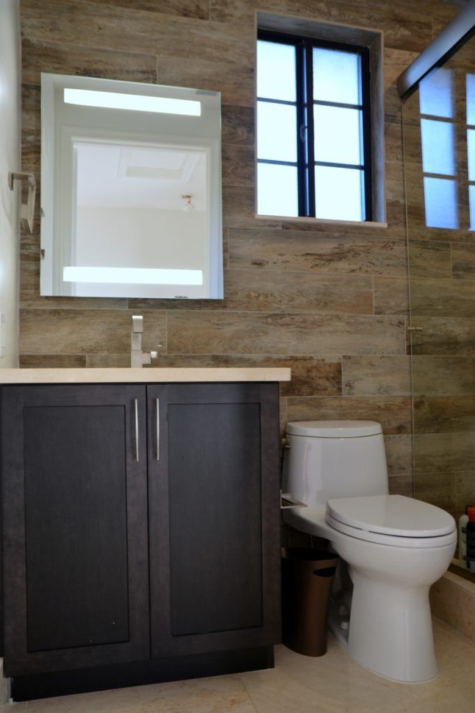 Bathroom with dark cabinet, white toilet, tiled wall, and window.