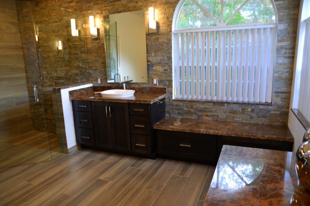 Bathroom with dark wood vanity, stone wall, and arched window with blinds.