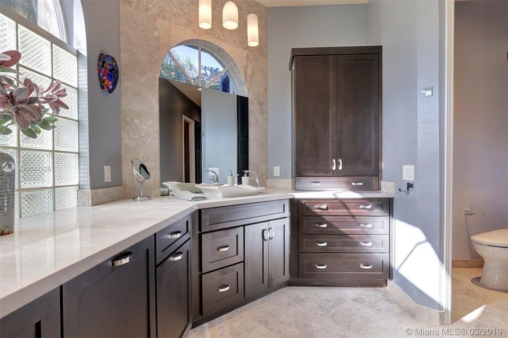 Bathroom with dark brown cabinets, white countertops, and a glass block window.