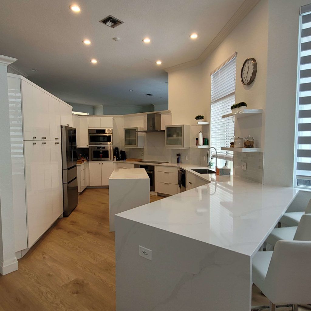 Bright modern kitchen with white cabinets, wood floor, and a glossy white island under recessed ceiling lights
