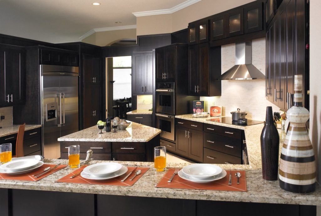 Modern kitchen with dark cabinets, granite island, set dining table, and stainless steel range hood