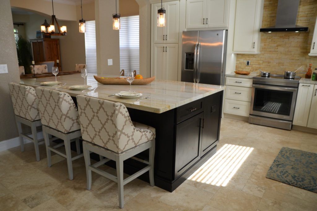 Bright kitchen with marble island, patterned barstools, stainless appliances, and sunlight on the floor