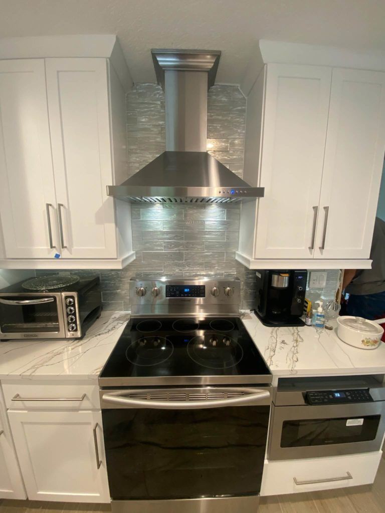 Modern white kitchen with stainless steel range hood, black stove, and built-in appliances
