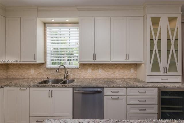 Bright white kitchen with marble counters, stainless dishwasher, sink, and glass-front cabinets