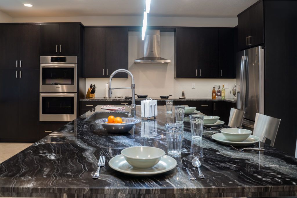 Modern kitchen with dark cabinets, marble island set with dishes and glassware