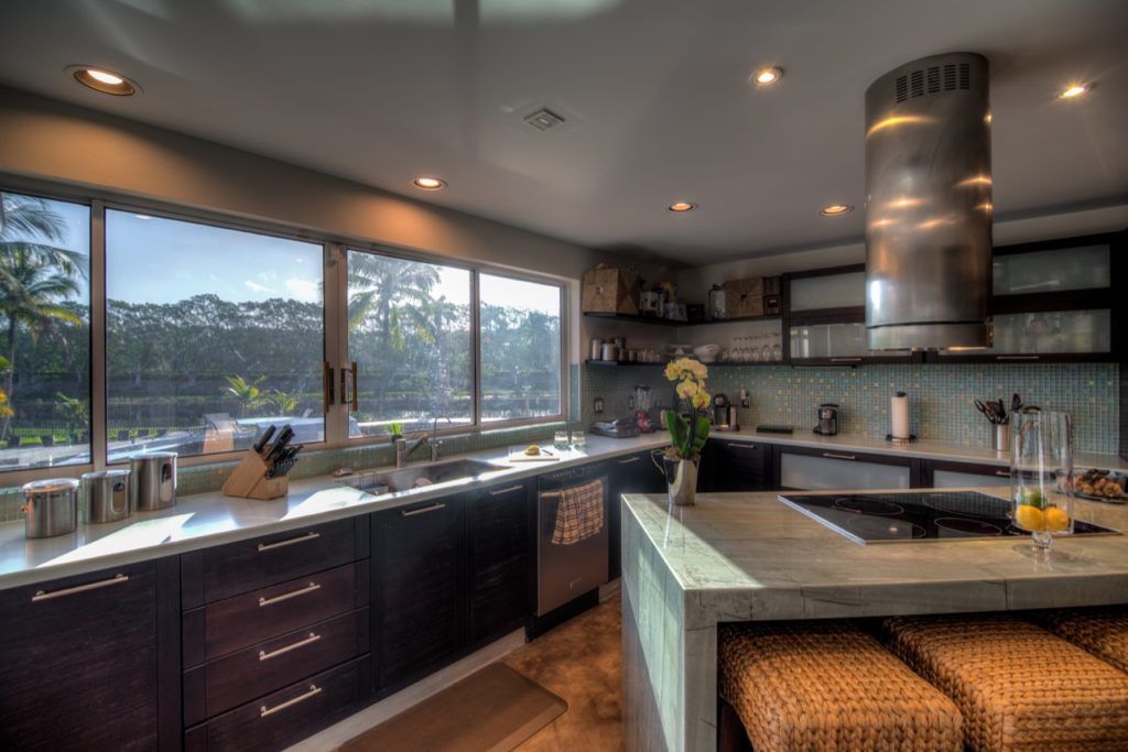 Modern kitchen with dark cabinets, large windows, and a central island with woven stools