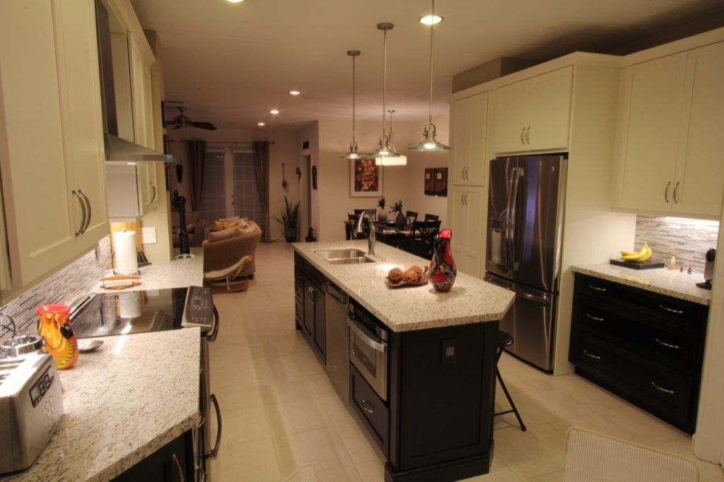 Modern kitchen with white cabinets, black island, granite counters, and pendant lights.
