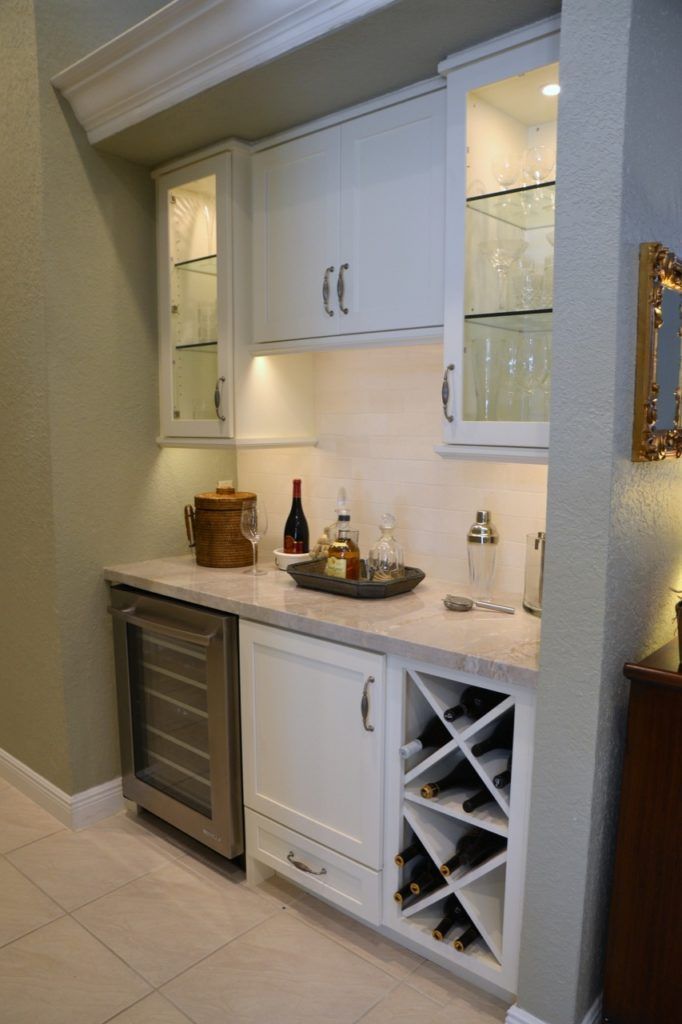 Built-in white home bar with wine rack, glass cabinets, and countertop decor in a hallway nook