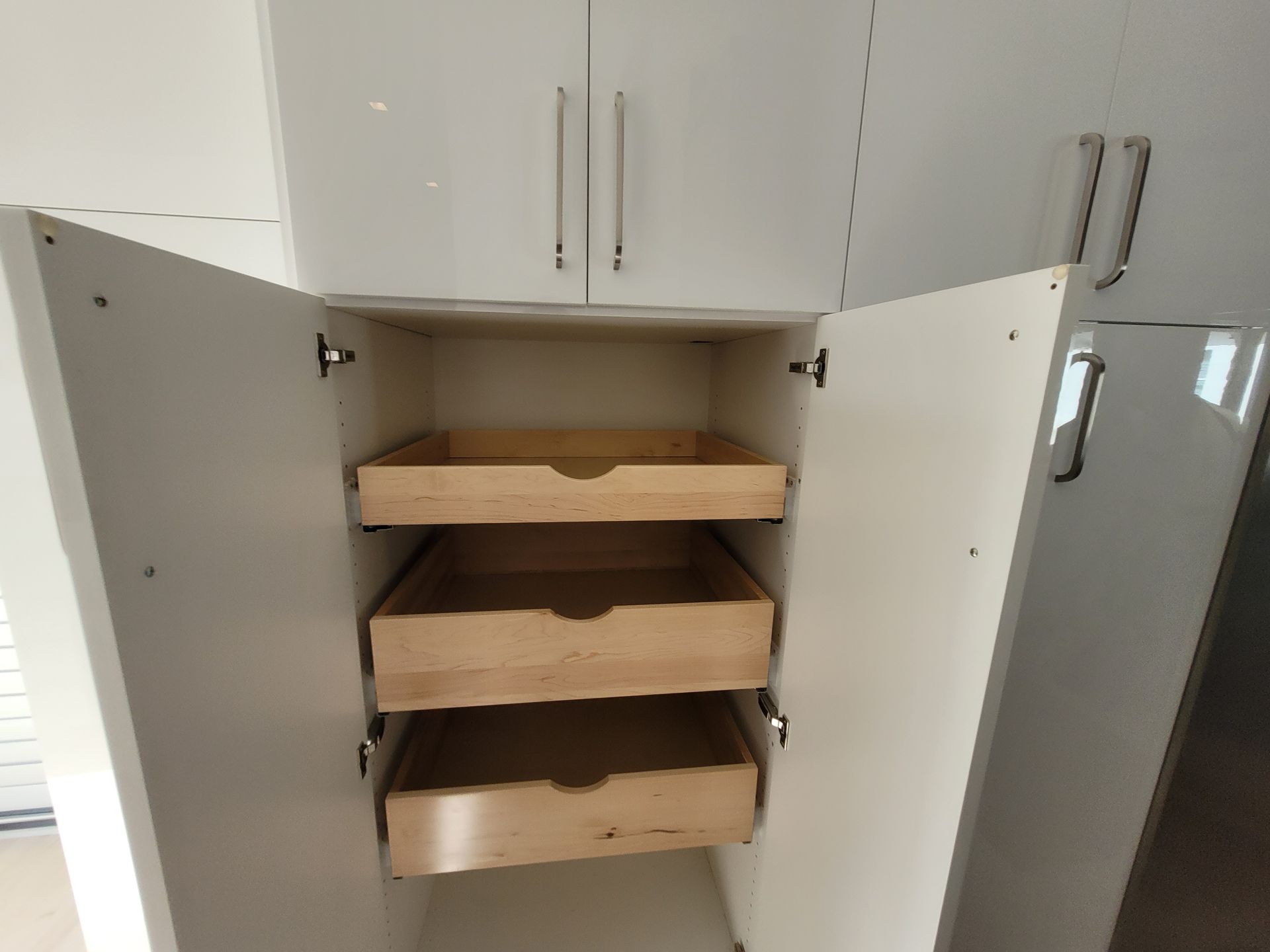 Open cabinet with three wooden pull-out shelves in a white kitchen