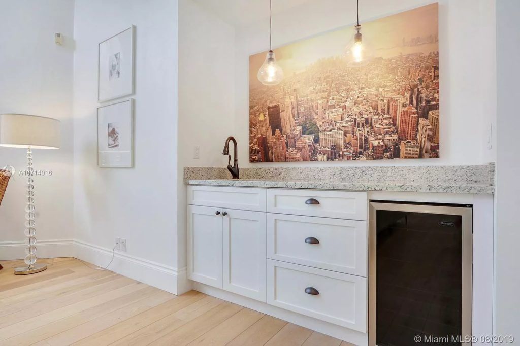 Bright white kitchen counter with sink, black faucet, cityscape wall art, and hanging pendant lights