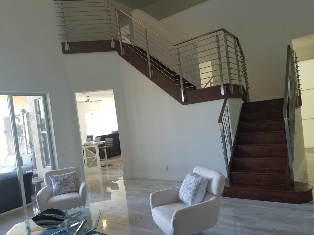 Modern living room with white chairs and a dark wood staircase with metal railing.