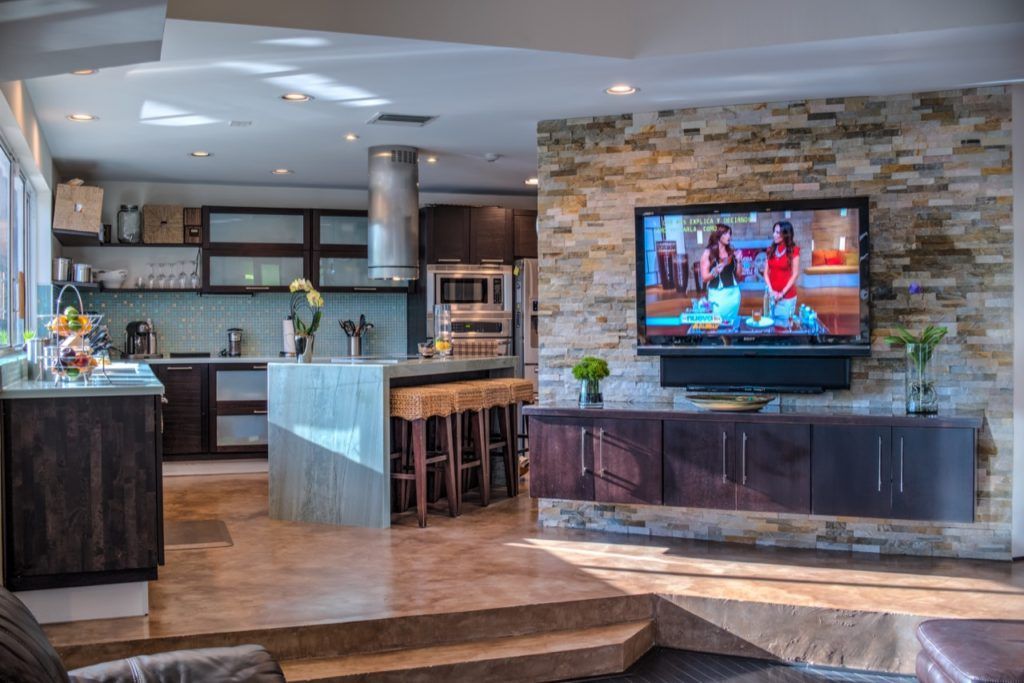 Modern kitchen and living room with stone fireplace, wall-mounted TV, and island seating