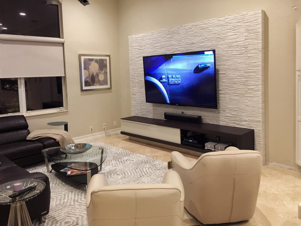 Modern living room with wall-mounted TV, beige chairs, glass table, and textured accent wall
