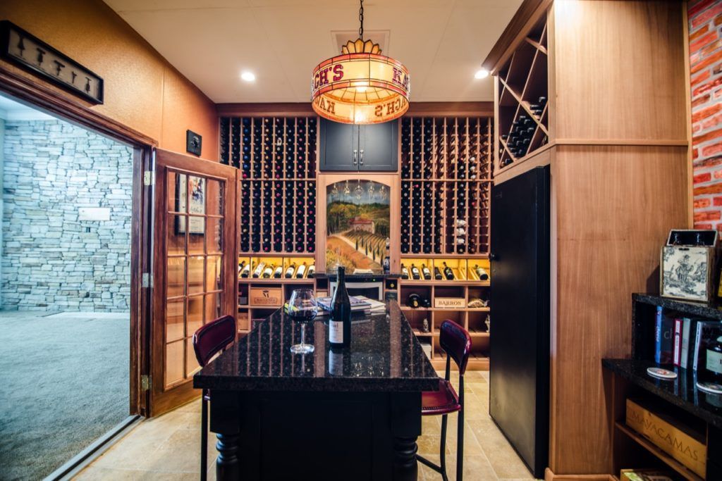 Warm, wood-paneled dining room with a central table, wine racks, and a chandelier above.