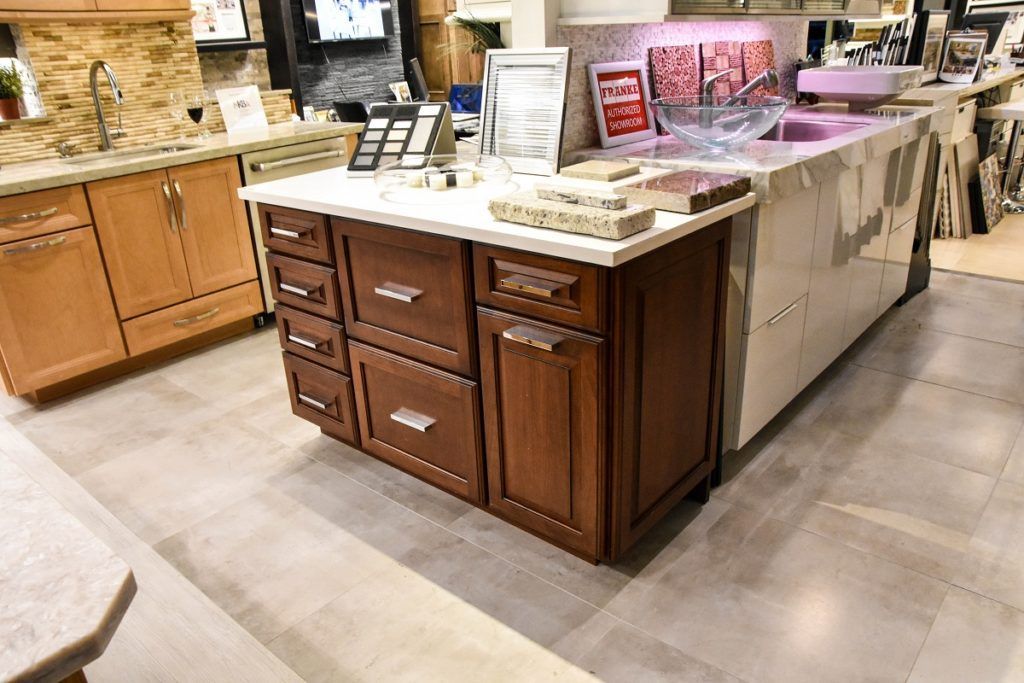 Stone and wood kitchen island display with drawers, marble countertop, and product samples in a showroom