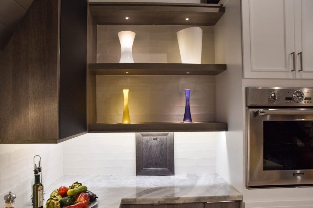 Modern kitchen with open shelves, white vases, and colorful glass decor beside a built-in oven