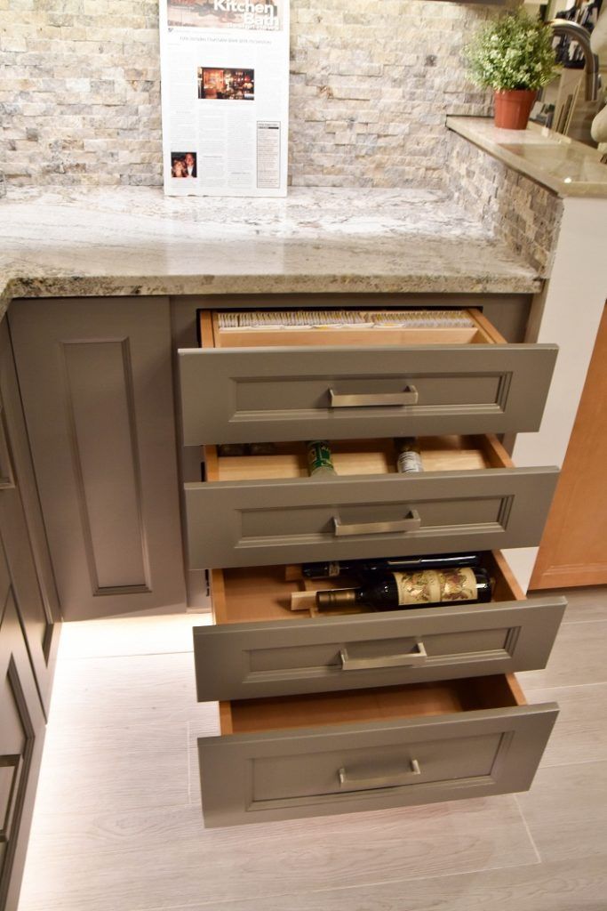 Kitchen cabinet with four open drawers under a stone countertop, showing packaged food inside.