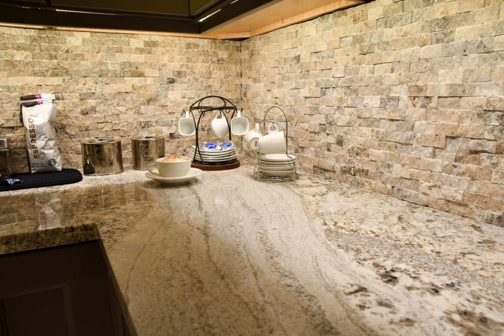 Granite kitchen countertop with stone tile backsplash, coffee maker, jars, and dish rack under warm lighting