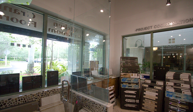 Empty storefront interior with glass entrance, brochure rack, and stacked boxes near the wall.