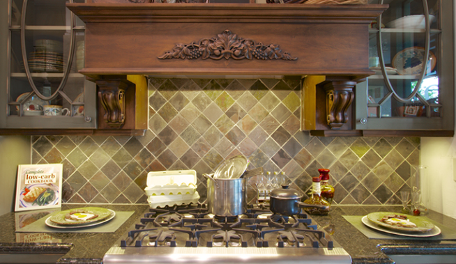 Kitchen stove with copper pot, tiled backsplash, wooden hood, and decorative shelves