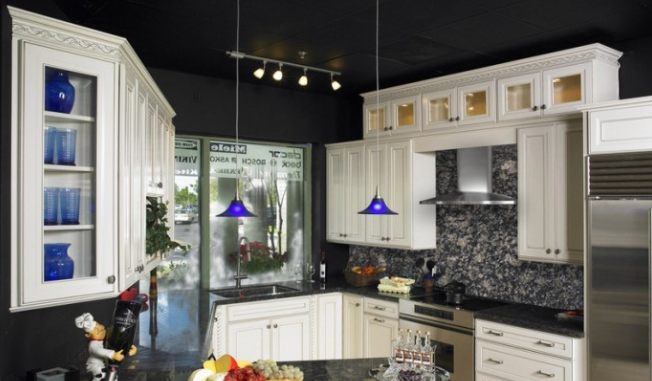 Modern kitchen with black countertops, white cabinets, blue pendant lights, and a mosaic tile backsplash