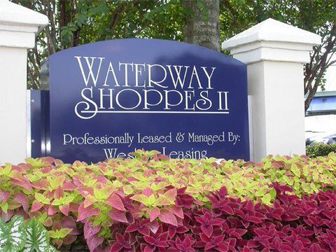 Waterway Shoppes II sign behind pink and green shrubs at an outdoor entrance