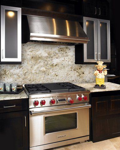 Modern kitchen with stainless steel stove, range hood, dark cabinets, and granite backsplash.