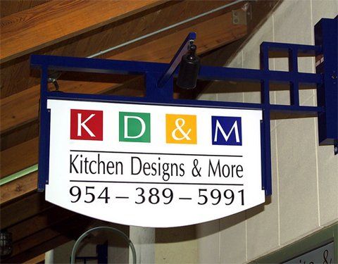 Sign for K D & M Kitchen Designs & More with phone number 954-389-5991 hanging indoors