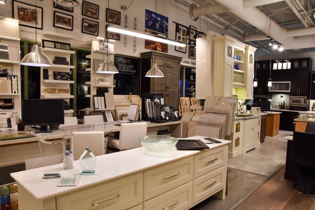 Bright kitchen showroom with white island, pendant lights, cabinets, and wood flooring