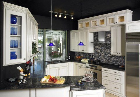 Modern white kitchen with black countertops, mosaic backsplash, stainless fridge, and central island