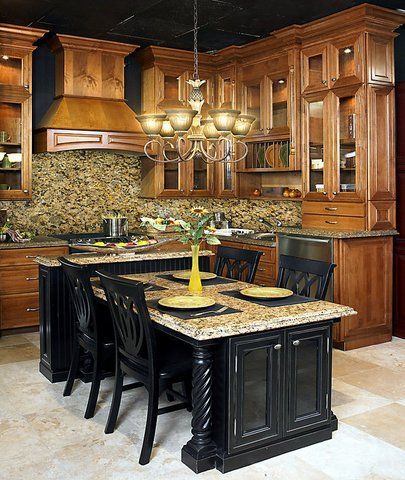 Elegant kitchen with wood cabinets, granite island, black chairs, and a hanging chandelier.