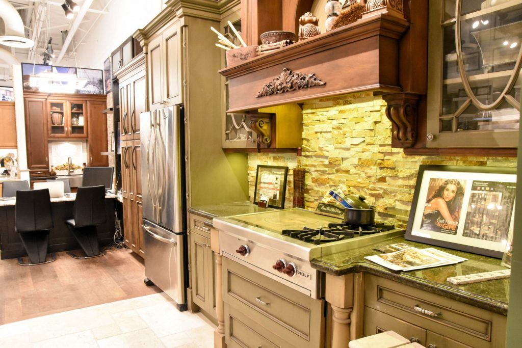 Warm-toned kitchen with ornate cabinetry, tiled backsplash, and dining area in the background.