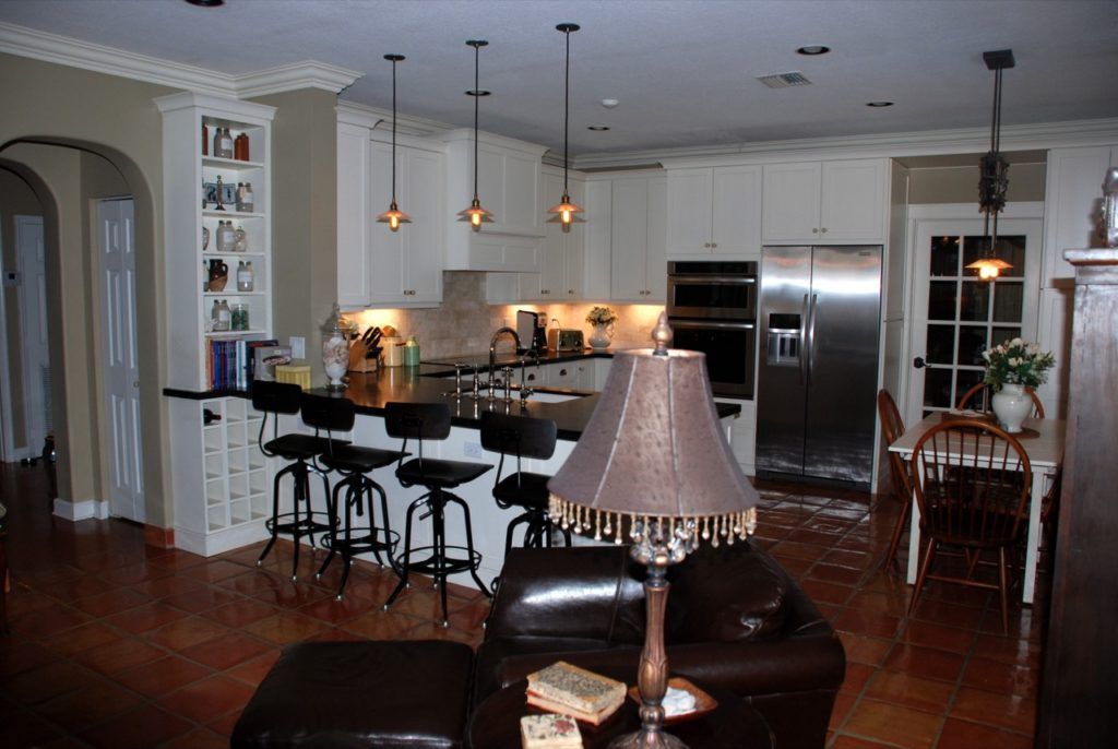 Modern kitchen with white cabinets, black bar stools, stainless fridge, and hardwood floors